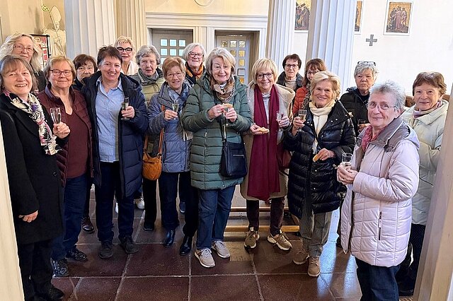 Gruppe von Frauen in Winterkleidung steht in einem hellen Raum und hält Sektgläser in der Hand