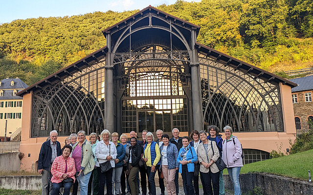 Eine Gruppe aus Frauen und Männern steht bei herbstlichem Wetter vor einer Industriehalle, der ehemaligen Gießhalle der Sayner Hütte, und schaut in Richtung der Betrachtenden. Eine Gruppe aus Frauen und Männern steht bei herbstlichem Wetter vor einer Industriehalle, der ehemaligen Gießhalle der Sayner Hütte, und schaut in Richtung der Betrachtenden.