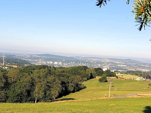 Aufnahme mit Blick von Berg Moriah über das Tal mit einer Weide im Vordergrund und einer Baumreihe, die sich von der linken Seite zur Bildmitte zieht.