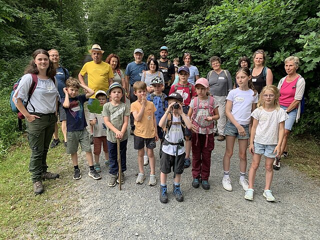 Gruppe von Erwachsenen und Kindern steht auf einem Waldweg, umgeben von dichtem Grün