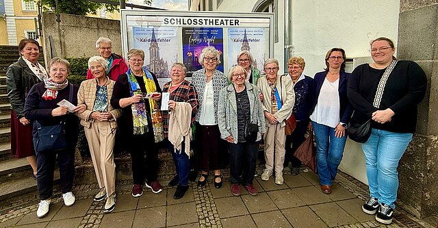 Eine Gruppe von Frauen steht vor einem Theatergebäude mit Plakaten in einem Schaukasten
