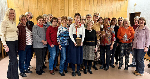Eine Gruppe von Frauen steht in einem Raum mit Holzvertäfelung, zwei Frauen halten jeweils eine kleine Statue