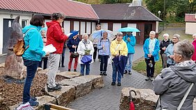 Eine Gruppe Frauen steht mit Regenschirmen und Jacken bei einem meditativen Abendspaziergang vor einem Fachwerkgebäude