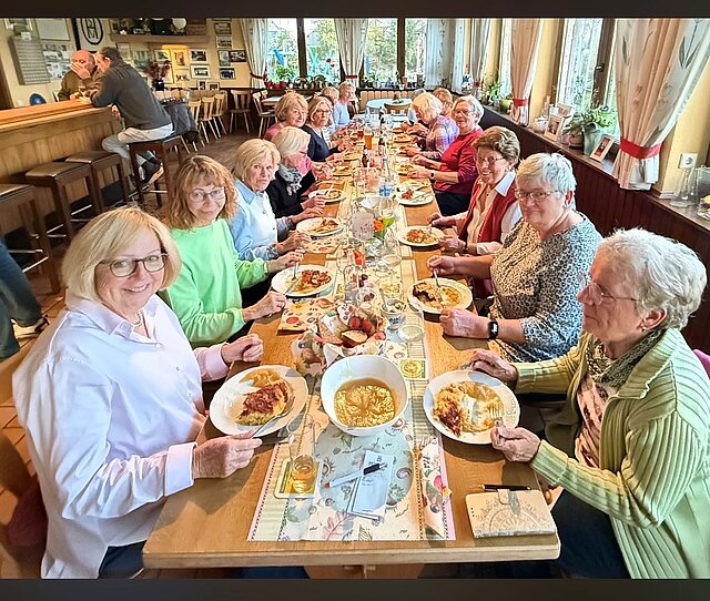 Gruppe älterer Frauen sitzt an einem langen Tisch in einem Restaurant und isst gemeinsam Döppekooche von Tellern.