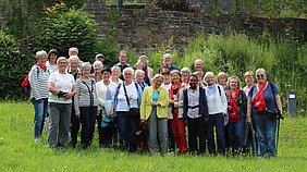 Gruppe von Erwachsenen steht auf einer Wiese vor einer alten Steinmauer im Naturerlebnispark