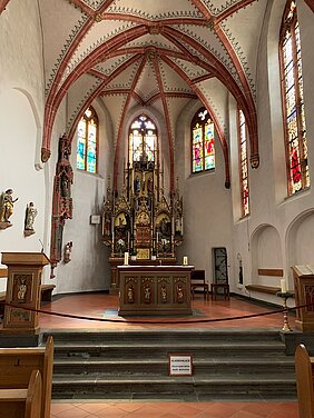 Innenraum einer Kirche mit gotischem Gewölbe, Altar mit Kerzen und bunten Glasfenstern
