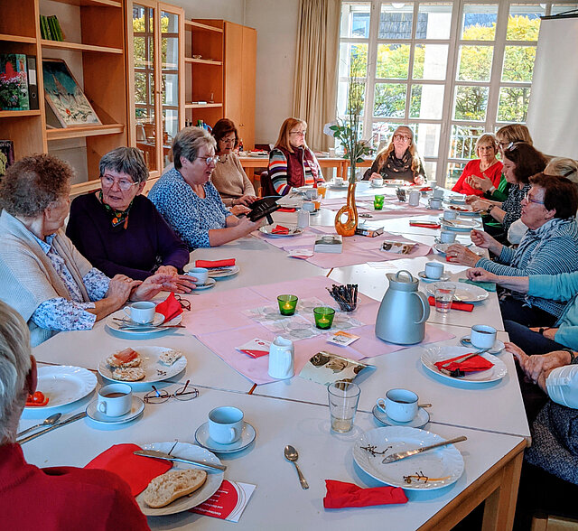 Mehrere Frauen sitzen an einem großen, rechteckigen Tisch mit weißem Geschirr, roten Servietten und Gläsern.